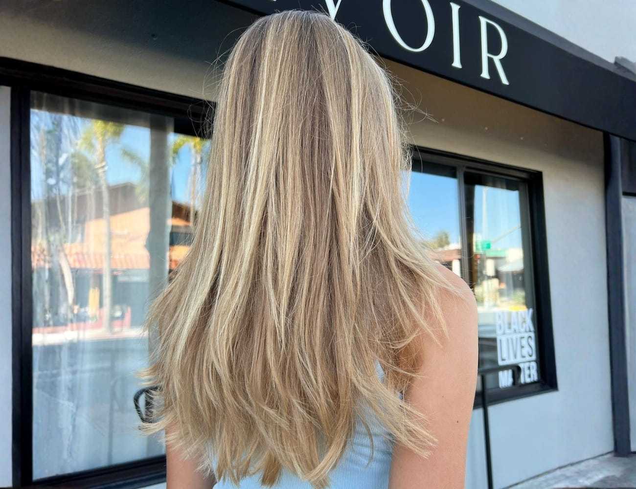 Blonde woman facing storefront, hair flowing naturally in front of a shop window.