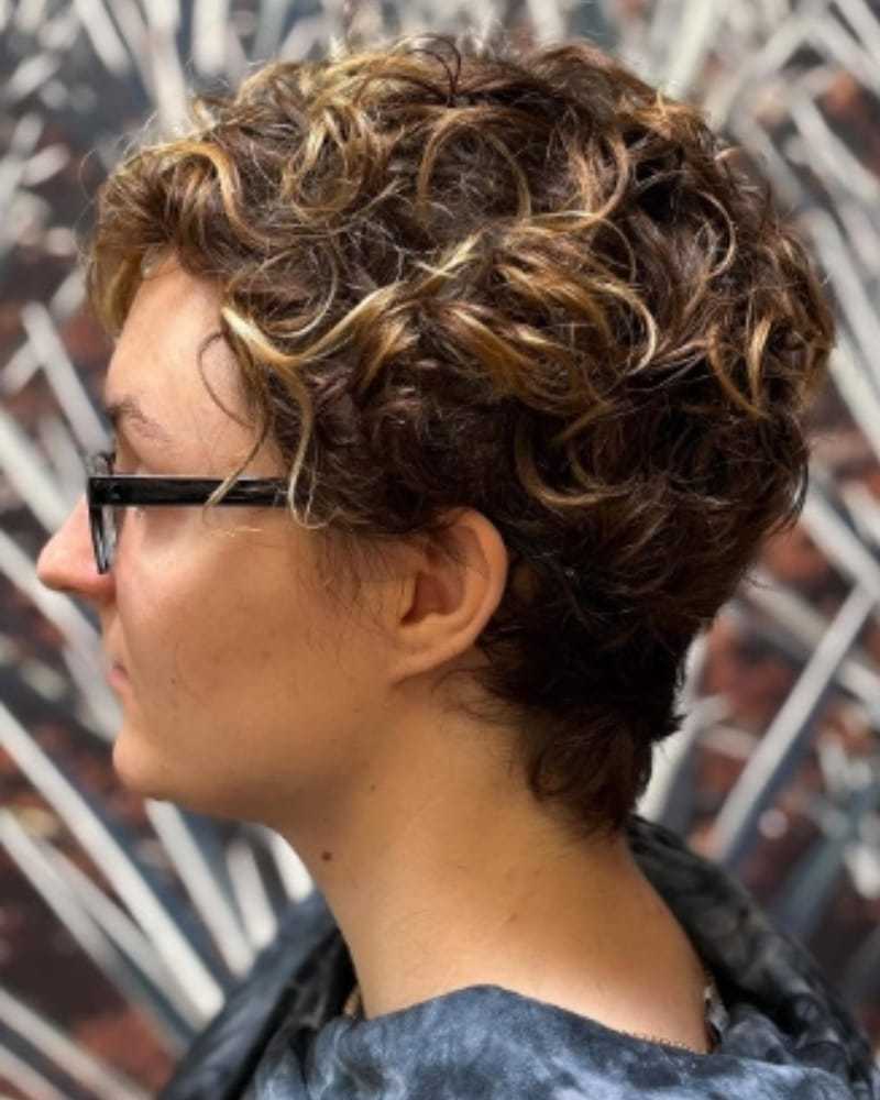 Person with short curly hair and glasses, side profile against a blurred background.