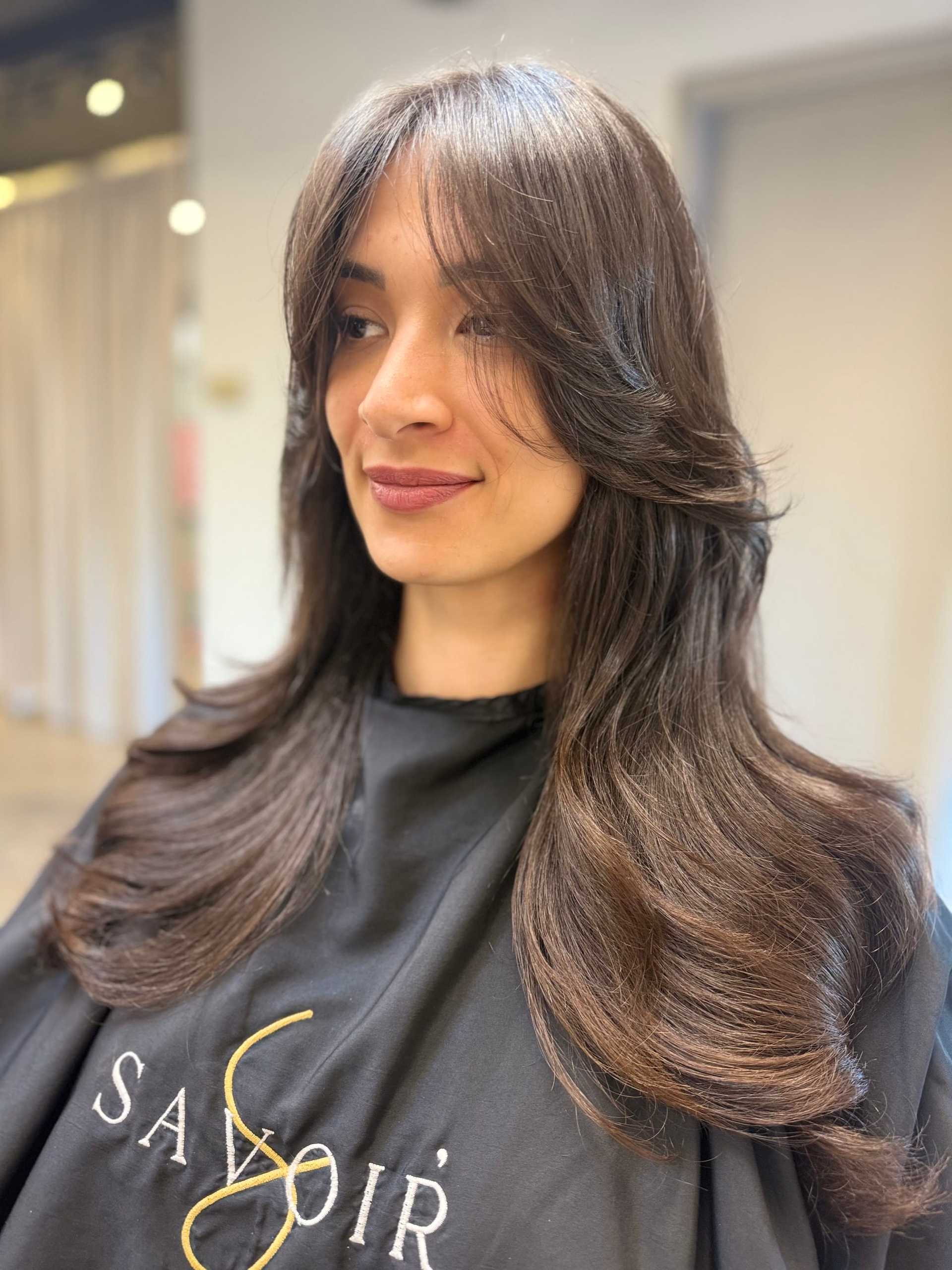 Woman with long, wavy hair styled in salon, wearing a black salon cape.