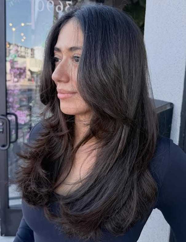 Woman with long, layered dark hair in a salon setting, wearing a black top.