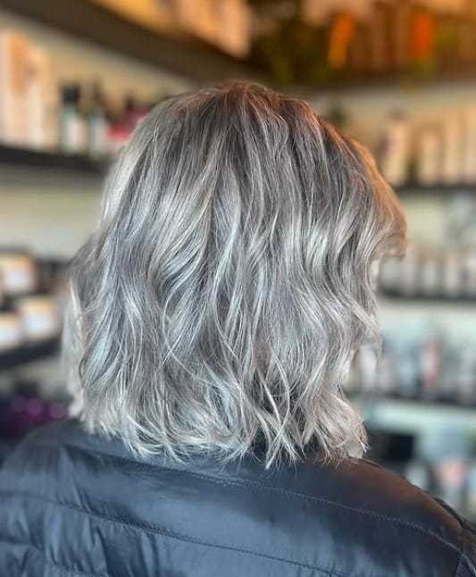 Grey wavy haircut with subtle highlights, displayed from the back, in a salon setting.
