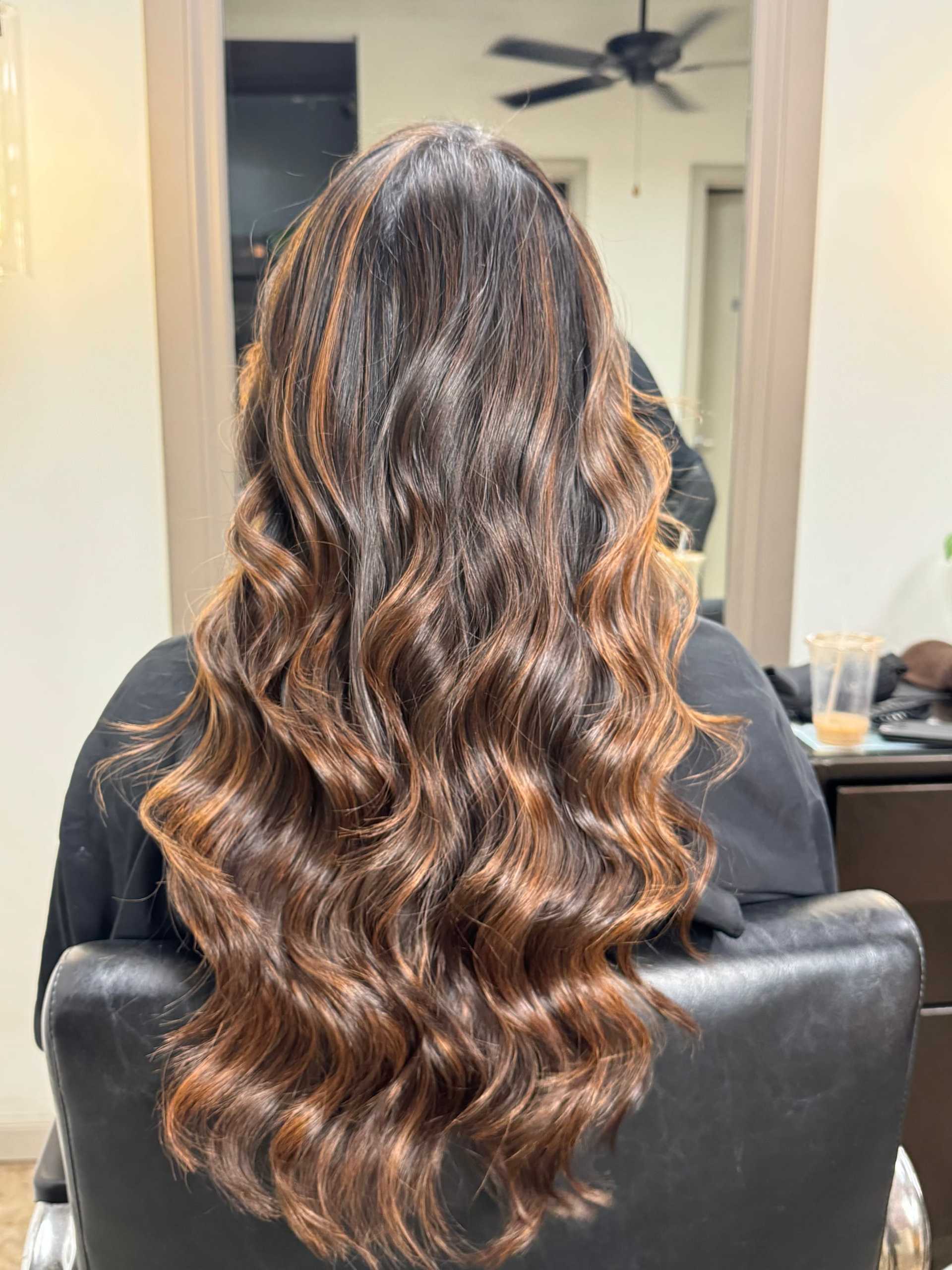 Long wavy hair with brown highlights in a salon chair, reflecting light.