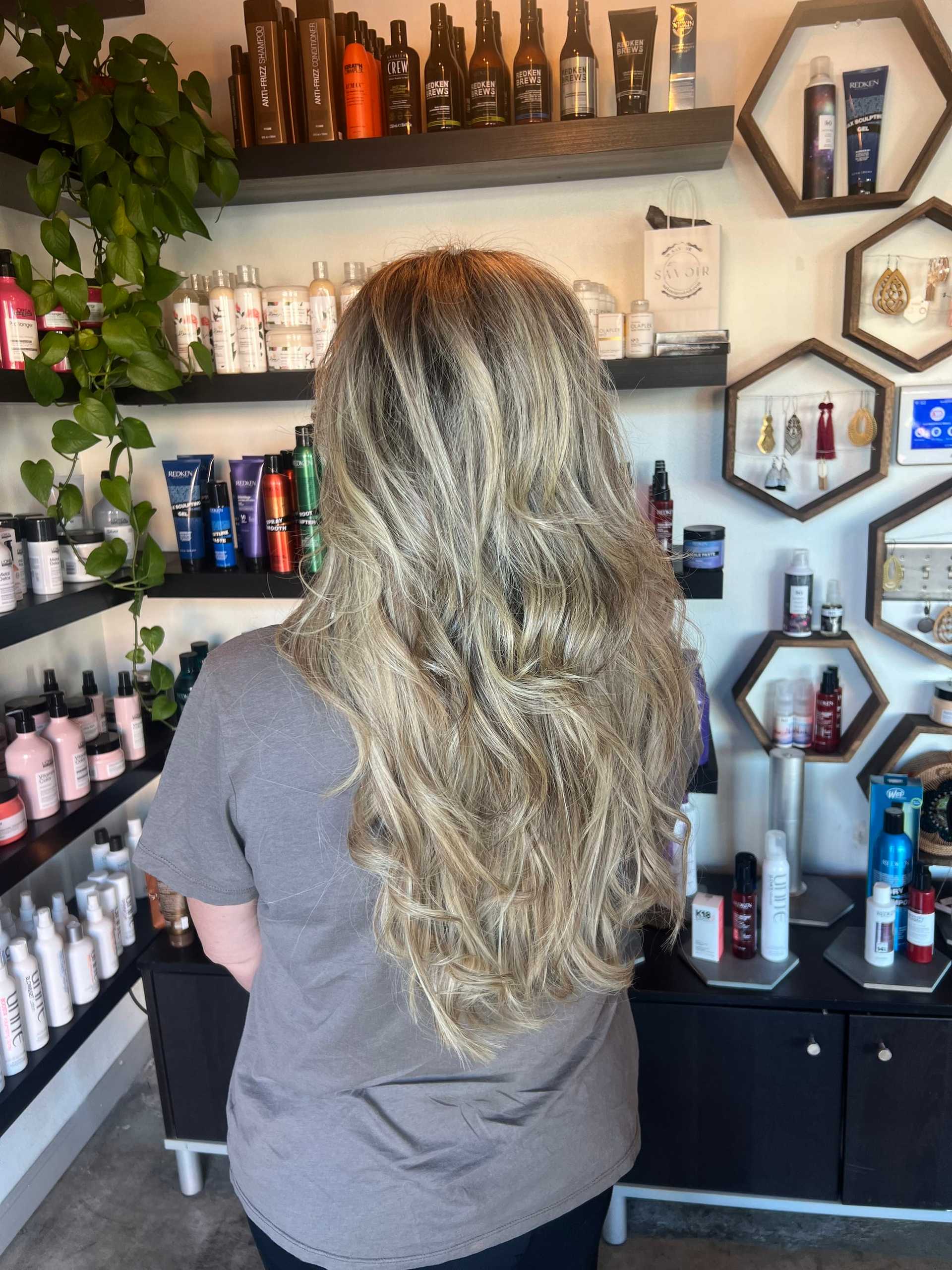 Long, wavy blonde hair in salon with shelves of hair products in the background.