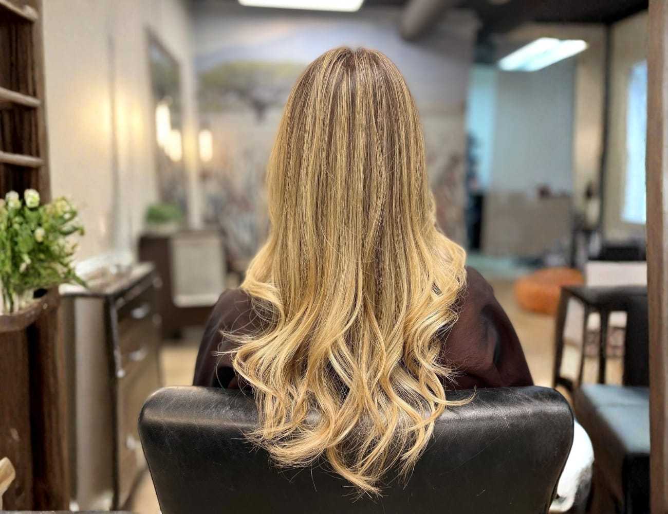Blonde woman with long, wavy hair sitting in a stylish salon chair.