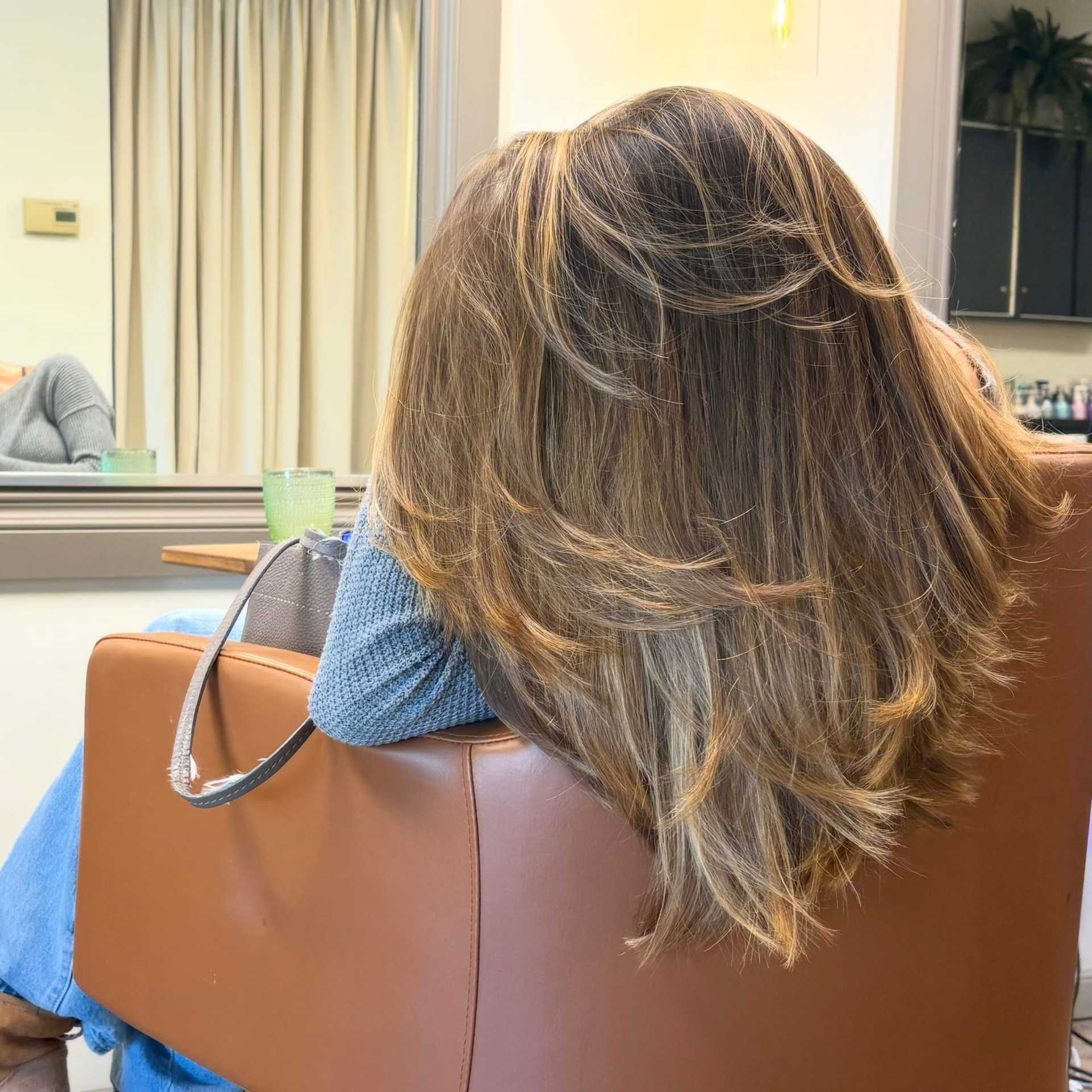 Woman with styled, medium-length hair sits in a salon chair, facing away.