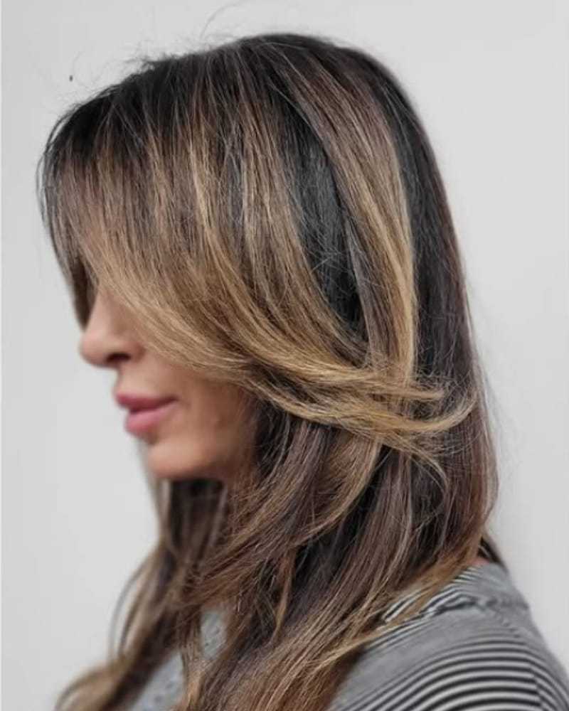 Woman with layered brown hair featuring blonde highlights, in a side profile view.