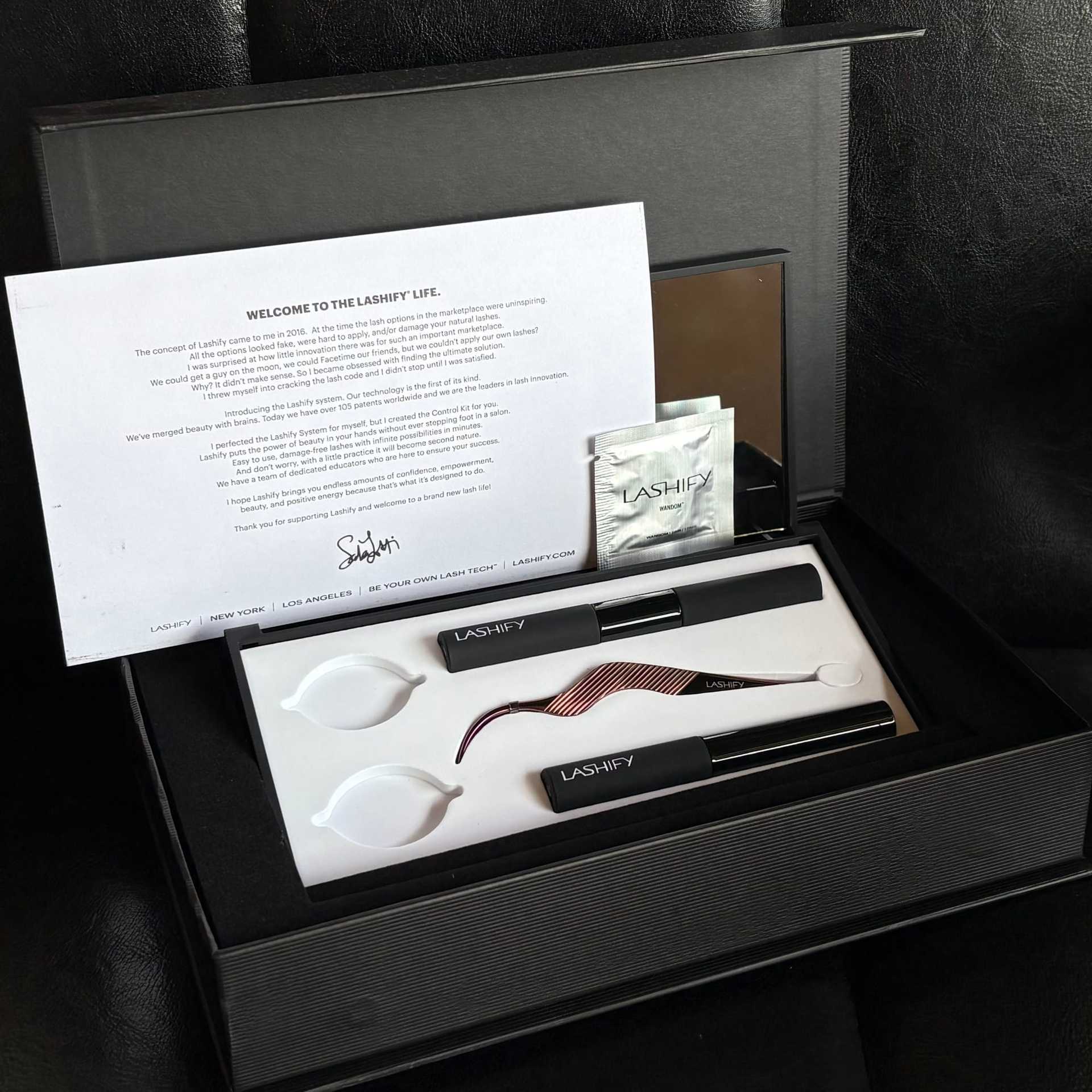 Eyelash kit with instructions, applicator, lashes, and adhesive on a black background.