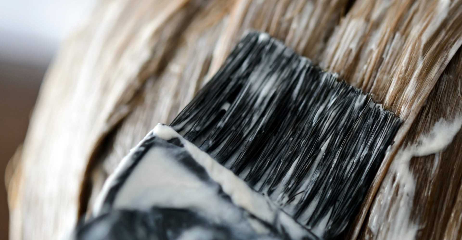 Hairbrush applying dye to blonde hair strands, close-up.