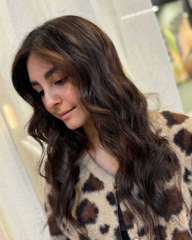Young woman with wavy brown hair and leopard-patterned cardigan against a light background.