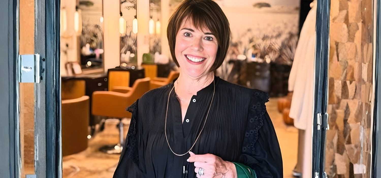 Woman smiling in stylish hair salon with warm, inviting decor.