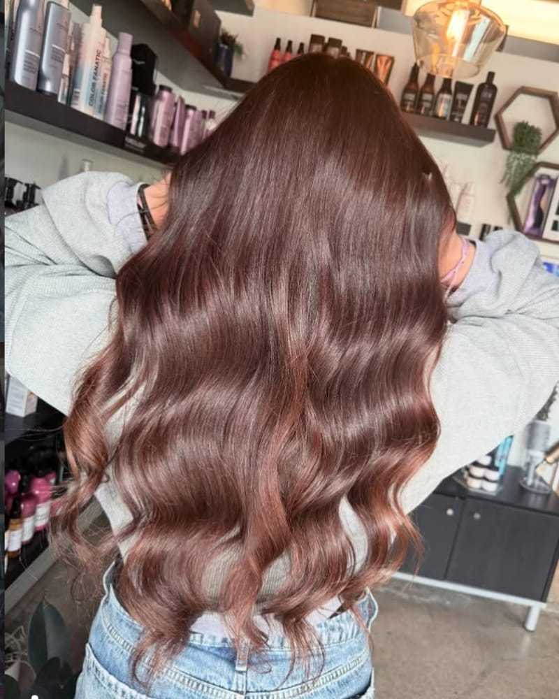 Long, wavy brunette hair styled in a salon, with shelves of hair products in the background.
