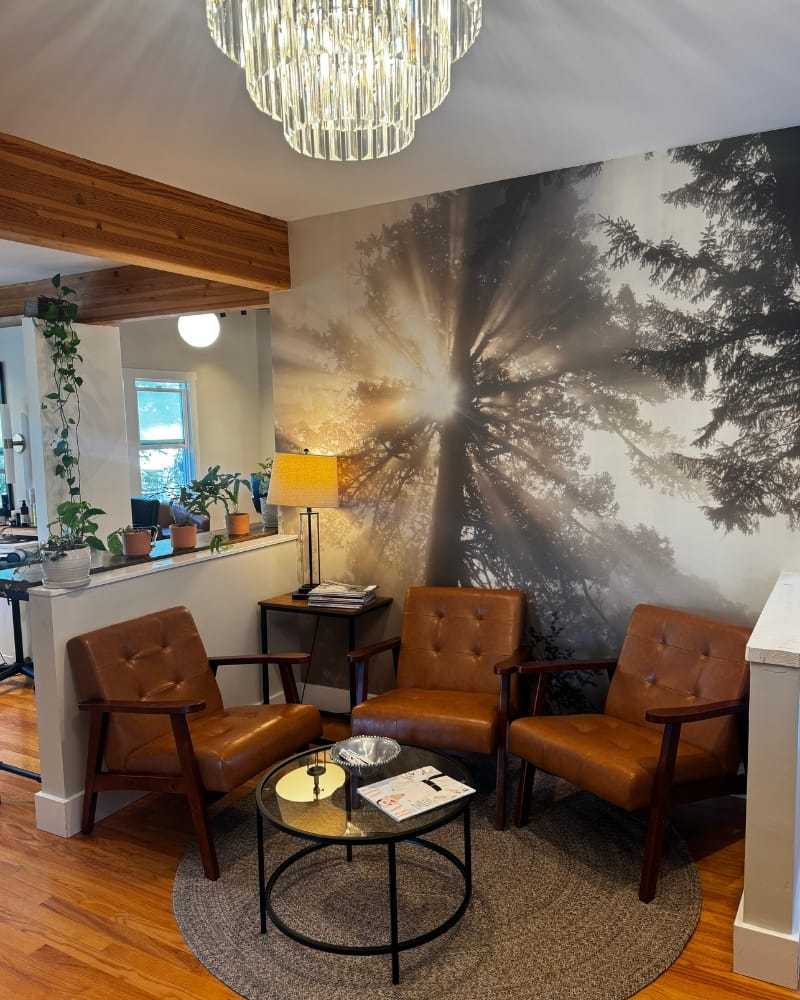 Cozy waiting area with leather chairs, coffee table, and forest-themed wall mural.