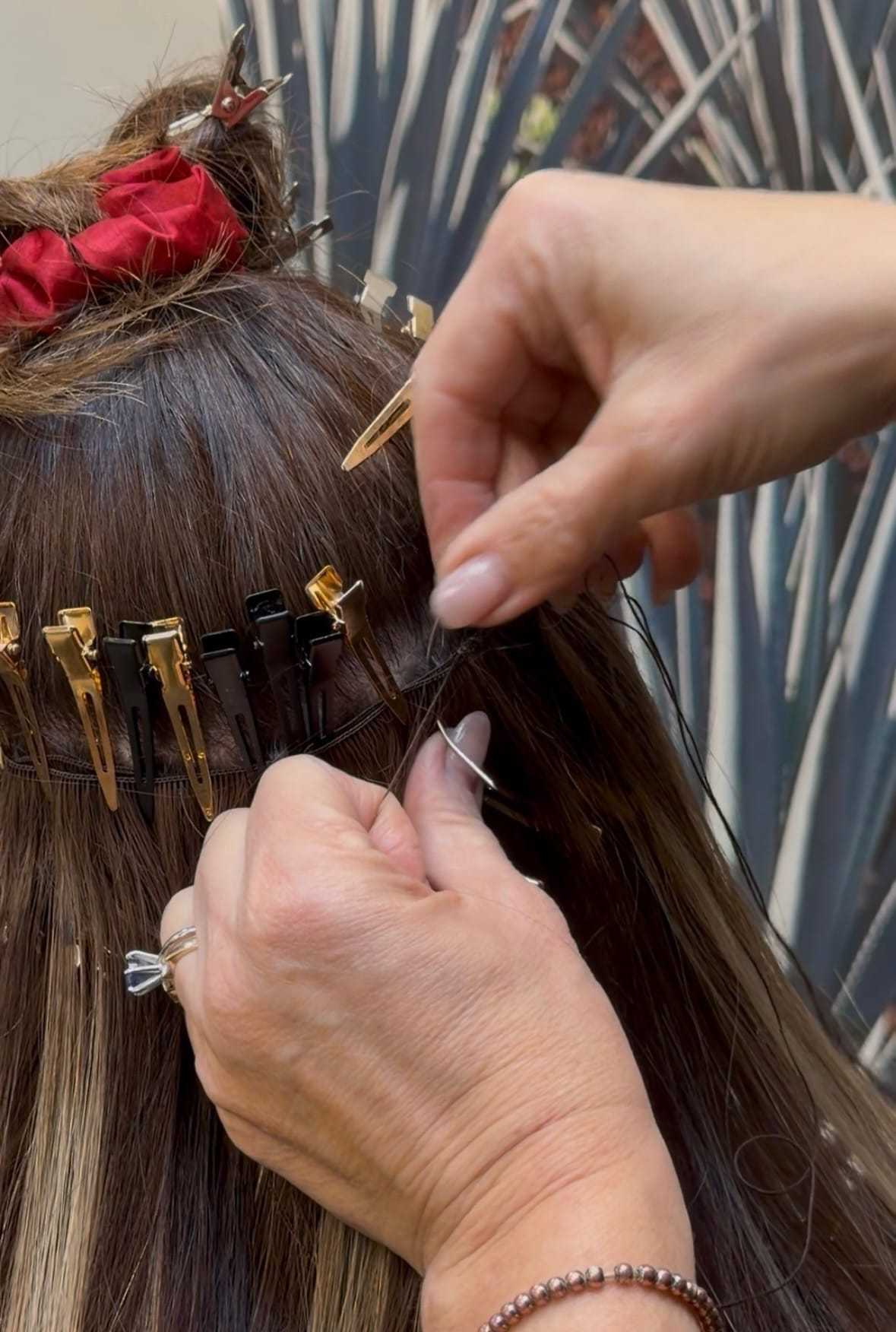 Hair extensions being applied to a woman's head using clips and thread.
